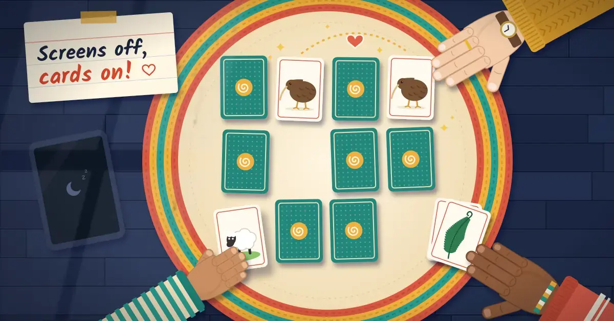 Illustration of a family playing a pairs memory game on a round braided rug on a rainy day, with a grandparent's hand in a mustard cardigan finding a matching pair of kiwi cards, a toddler sliding out a sheep card, a teenager resting a hand on a won pair of silver fern cards, a switched-off tablet nearby and a note reading "Screens off, cards on!"